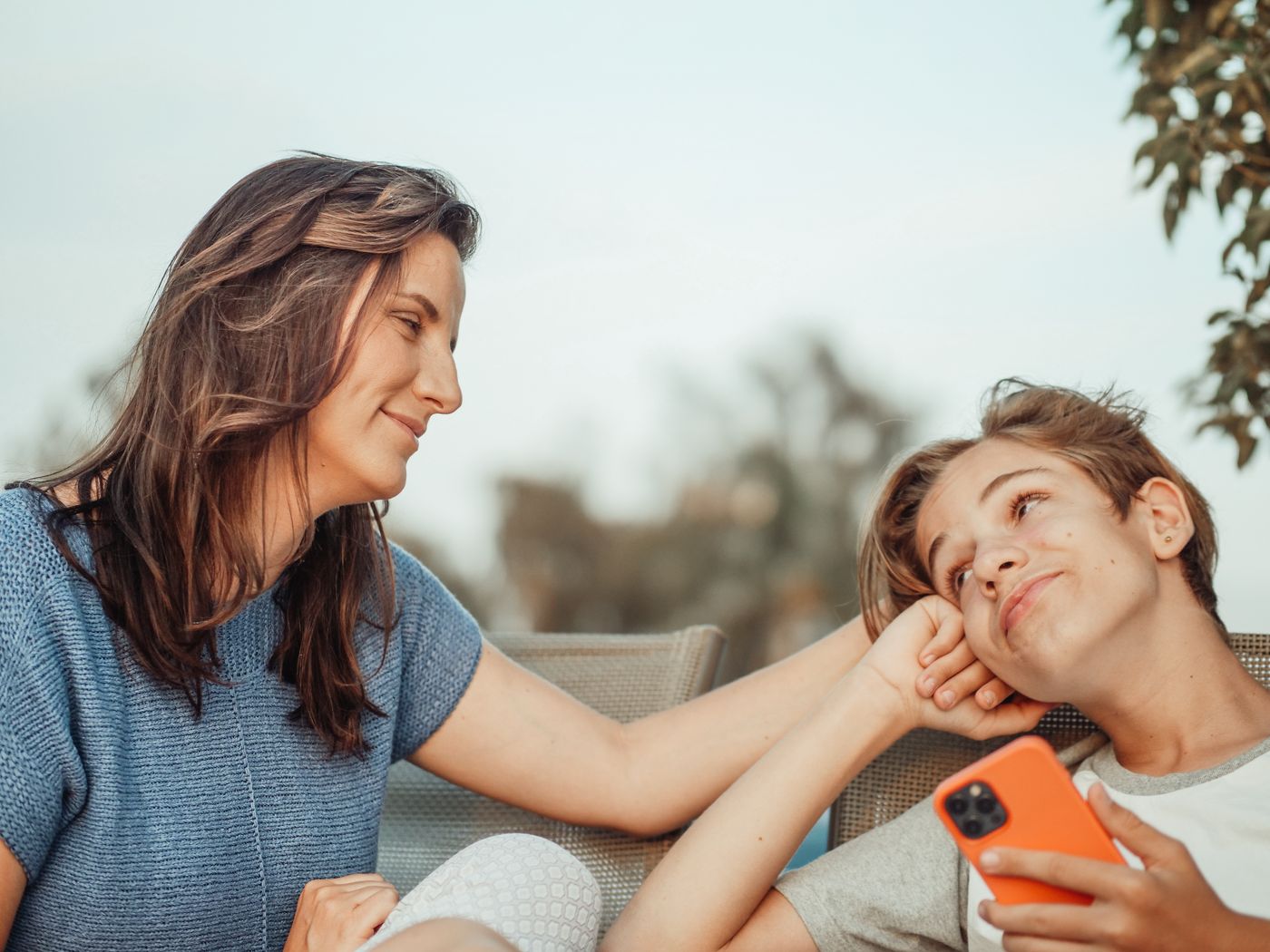 Mother and teenage son smiling at each other outdoors