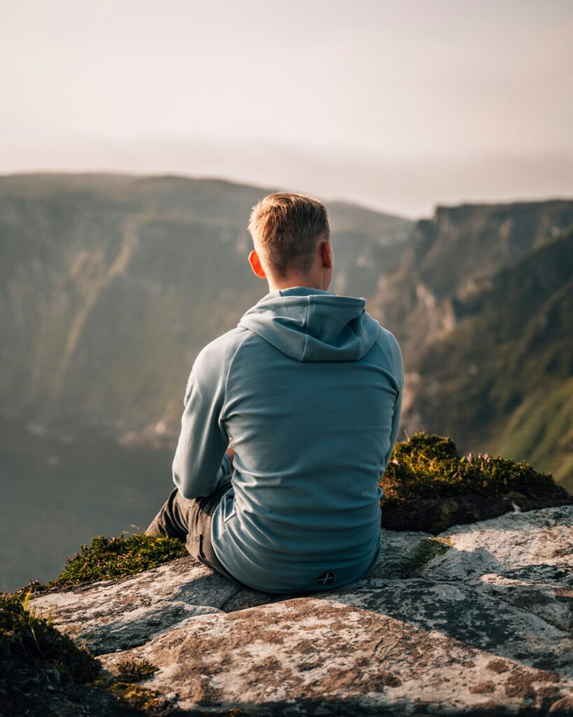 Man sitting calmly on a cliff edge looking out over a valley