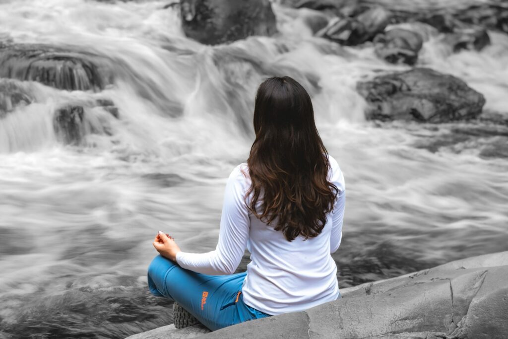 Woman meditating beside a rushing waterfall