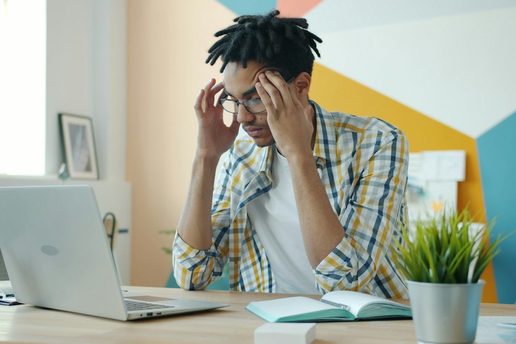 A frustrated young man at his desk holding his head in his hands